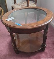 Full view of round end table showing glass top, wood rim, turned legs and lower shelf