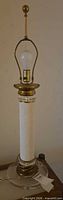 Full view of table lamp showing brass finial, harp, bulb, white textured column and clear glass base