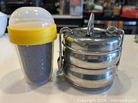 Tiffin stacked with latch frame alongside assembled plastic steamer cup