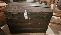 Front exterior of steamer trunk showing leather cover, metal straps, latch and wear