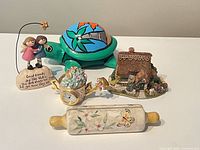 Group shot showing all five items: turtle trinket box, angel figurine, cottage model, floral clock, rolling pin holder