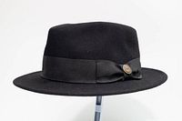 Side view of black wool fedora showing flat brim, grosgrain band, bow, and castle pin