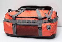 Front view of orange K3 duffel showing mesh pocket, logo crest, top flap, grey straps
