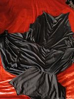 Full view of black cape spread out on red surface showing jagged hem and collar