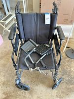 Front view of black Evermed transport wheelchair with detached footrests placed on seat
