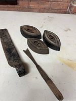 Lot overview showing three sad irons, pry bar piece and wood-handled scraper