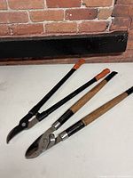 Two manual loppers displayed on white surface against brick wall background