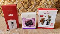 Front view of three Hallmark Star Wars ornament boxes: K-2SO, lunchbox, Wicket & Teebo