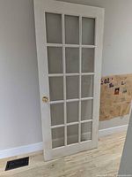 Full view of white French interior door showing 15 frosted glass panes, brass knob, and surface wear