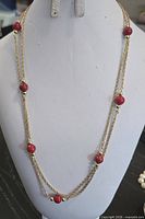 Full view of gold-tone chain necklace with red beads displayed on bust