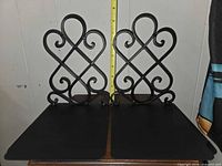 front view of both black scrollwork bookends against measuring tape