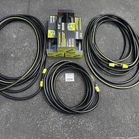 Three boxed Yardworks sprinklers between coiled black/yellow hoses