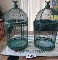 Front view of both teal metal birdcages on table