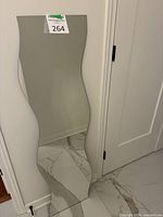 Front view of tall wavy-edge frameless mirror leaning against wall