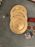 Four gold chargers with napkin ring boxes and bag visible
