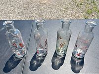 Front view of four clear glass vases with painted floral designs