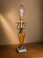 Full view of lamp showing glass body, marble base, metal feet, collar with prisms, harp and bulb