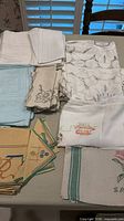 Grouped view of assorted folded tablecloths and napkins in various colours and embroidery