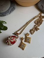 Necklace with red enamel egg pendant and pair of matching square earrings displayed together