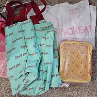 Group shot of all items: two aqua totes, white T-shirt, yellow pouch, partial view of pink and yellow totes
