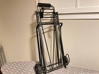 Full view of folded black metal luggage cart with two wheels