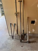 Group view of four yard tools leaning against wall