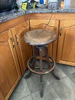 Single stool showing round wooden seat, four wooden legs, circular footrest, overall wear