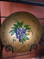 Front view of gold glass bowl showing grape artwork and script in stand