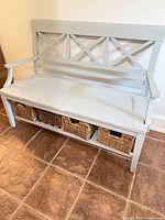 Front view of light gray wooden bench with three seagrass baskets in lower shelf