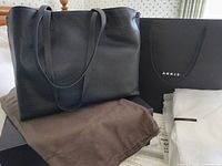 Front view of Akris black leather tote on dust bag with shopping bag, tissue and box visible