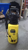 Front view of Karcher pressure washer showing yellow body, wheels, handle, hose and cord