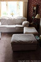 Couch and ottomans set in a living room setting near window with visible lighting from outdoors. Beige microfiber suede-like upholstery, shows some stains and wear.