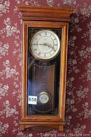 Full view of wooden pendulum wall clock with Roman numeral dial and visible pendulum.
