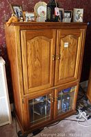 Front angled view of wooden TV cabinet showing upper wooden paneled doors and lower glass-paned doors with storage inside.