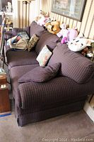 Left angled view of the brown plaid sofa with floral and patterned pillows, fabric upholstery, and stuffed animal toys placed on the backrest.