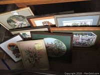 Eight framed cross stitch and needlepoint artworks stacked together showing variety of designs including floral, animals, and scenic themes.