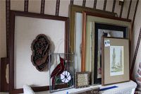 Overall view of framed wood carved dragonfly flower art, stained glass cardinal panel, cat print, two needlepoints, and other framed prints stored leaning against wall.