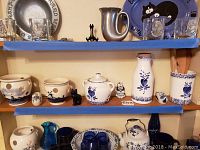 Shelf display of various blue and white ceramics, including potpourri holders and crock holder with wooden utensils, showing condition and decoration details