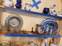 Shelf display with pewter mug, pewter plate with inscription, silver plate spoon and fork, teleflora plate, and four barware glasses.