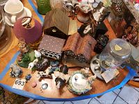 Top view of table with multiple small decorative items including bird feeder shaped music box, lamp with purple shade, assorted animal figurines, and decorative boxes.