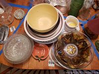Photo of assorted mixing bowls, glass serving bowls, gravy boat, and small divided dish on wooden table.
