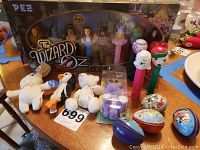 Wizard of Oz collector figures in box, plush toys, Pez dispensers, and metal eggs on table