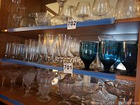 Shelved barware with various glasses including teal goblets, flutes, small wine glasses, and mugs along with a small picture frame, all showing ship pattern design.