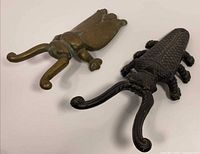 Brass and cast iron insect doorstops side by side showing material and finish differences