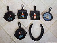 Five painted miniature skillets and horseshoe laid out