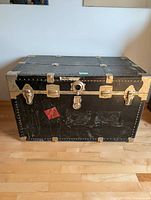 Front view of black steamer trunk with metal hardware