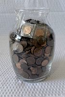 Front view of glass jar filled with pennies, tape seal visible