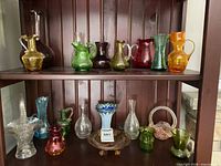 Shelf with eight colored glass pitchers and additional clear and colored glass decor pieces
