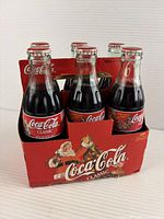 Front view of six unopened Coca-Cola bottles in carrier