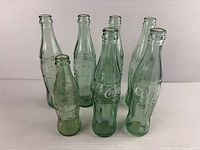 Group of seven green Coca-Cola contour bottles standing upright